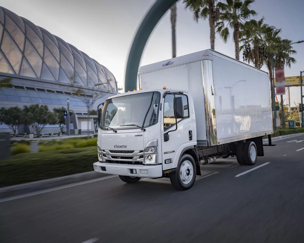 Isuzu commerical truck driving past large facility with palm trees.